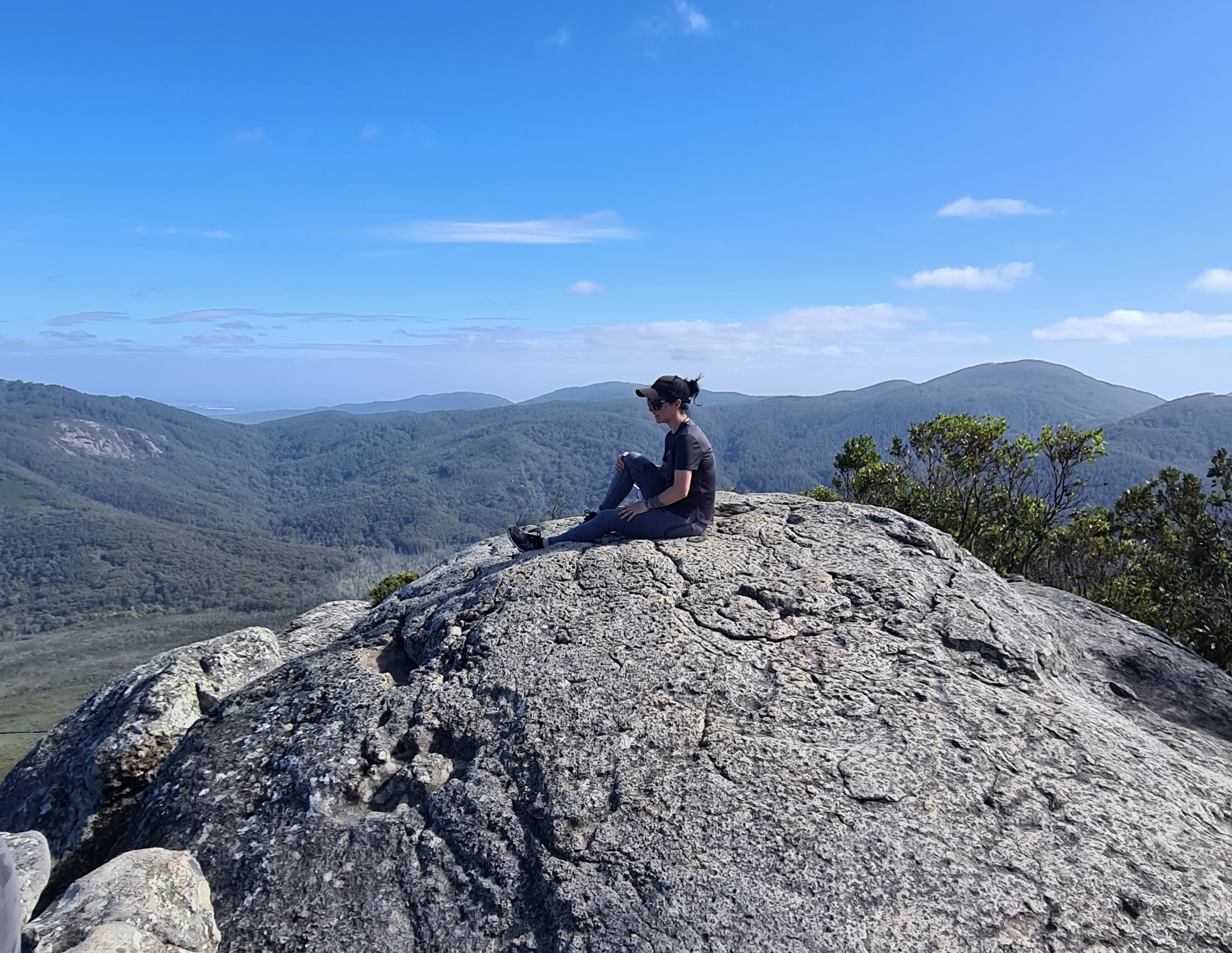 Courtney sitting contemplatively on a mountain rock overlooking vast landscapes
